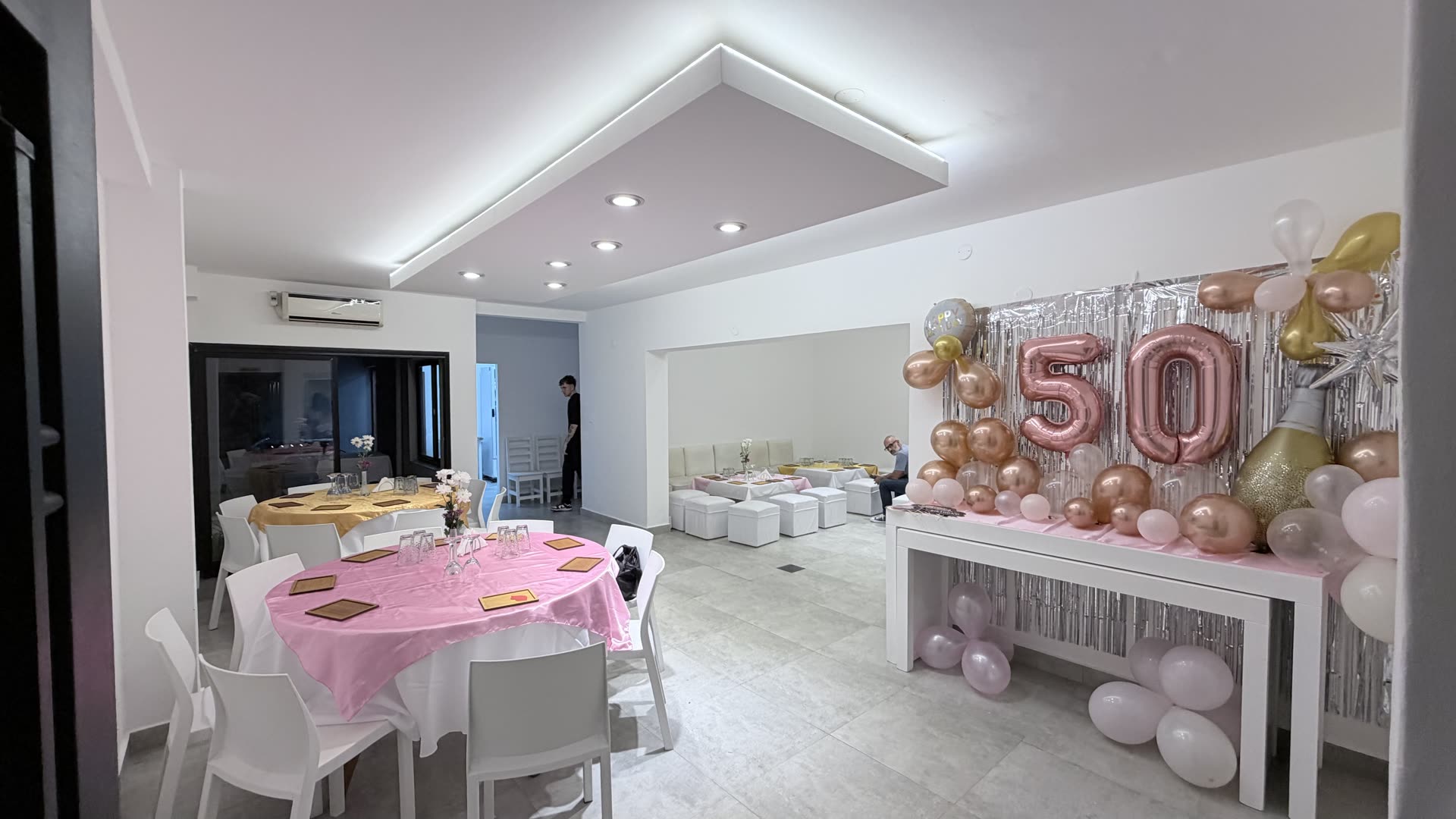 Salón armado para un cumpleaños de 50 con mesas, livings y decoración de globos